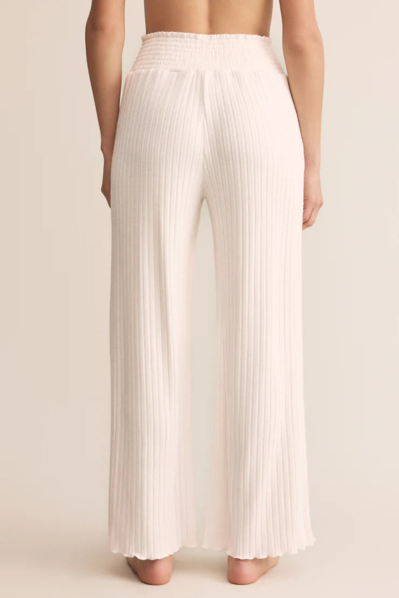 White pleated pants worn by a person on a beige background.