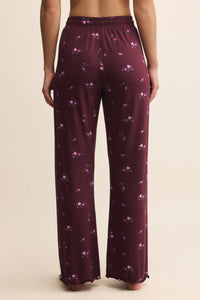 Maroon pajama pants with floral pattern worn by a person on a beige background.