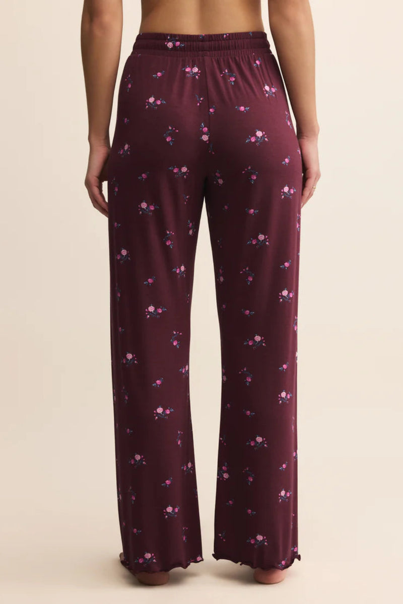 Maroon pajama pants with floral pattern worn by a person on a beige background.
