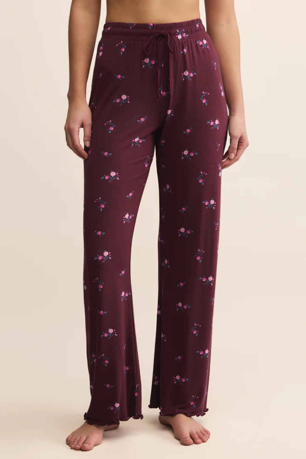 Purple pajama pants with floral pattern worn by a person on a beige background.