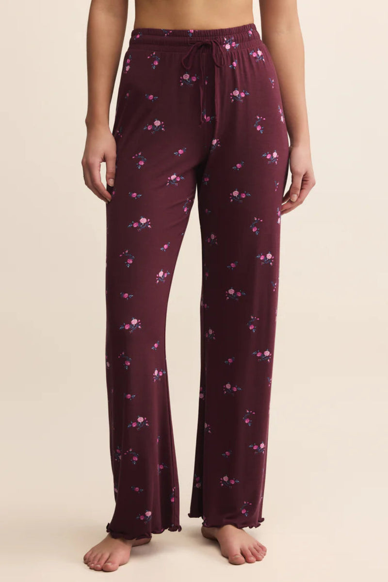 Purple pajama pants with floral pattern worn by a person on a beige background.