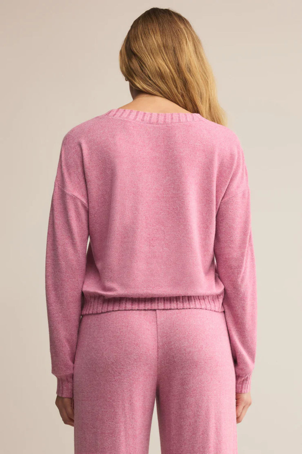 Person wearing a pink sweater and pants set against a neutral background.