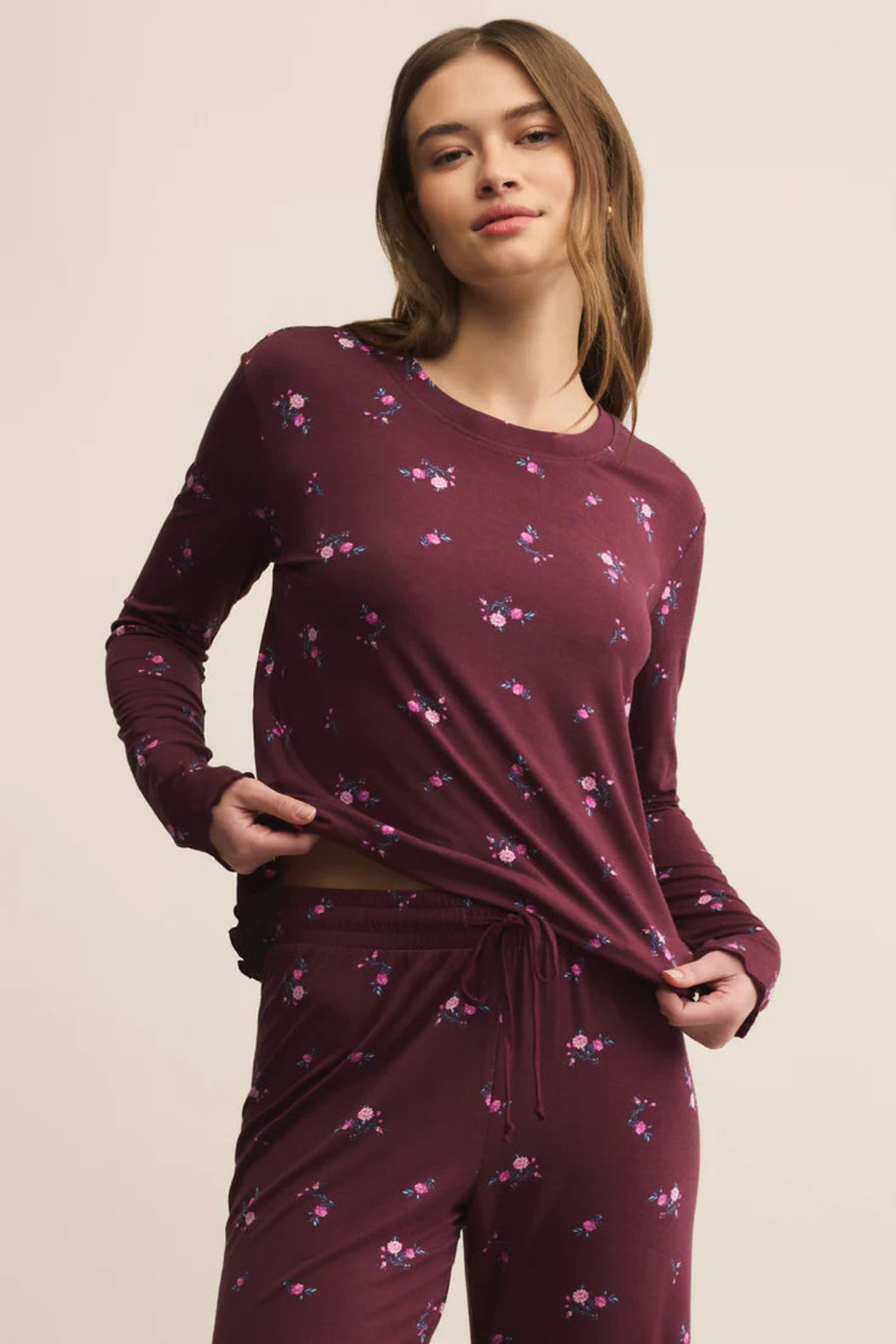 Woman wearing a burgundy long-sleeve top and pants with a subtle pattern on a beige background.