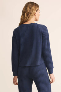 Woman wearing a blue ribbed sweater and pants on a beige background.