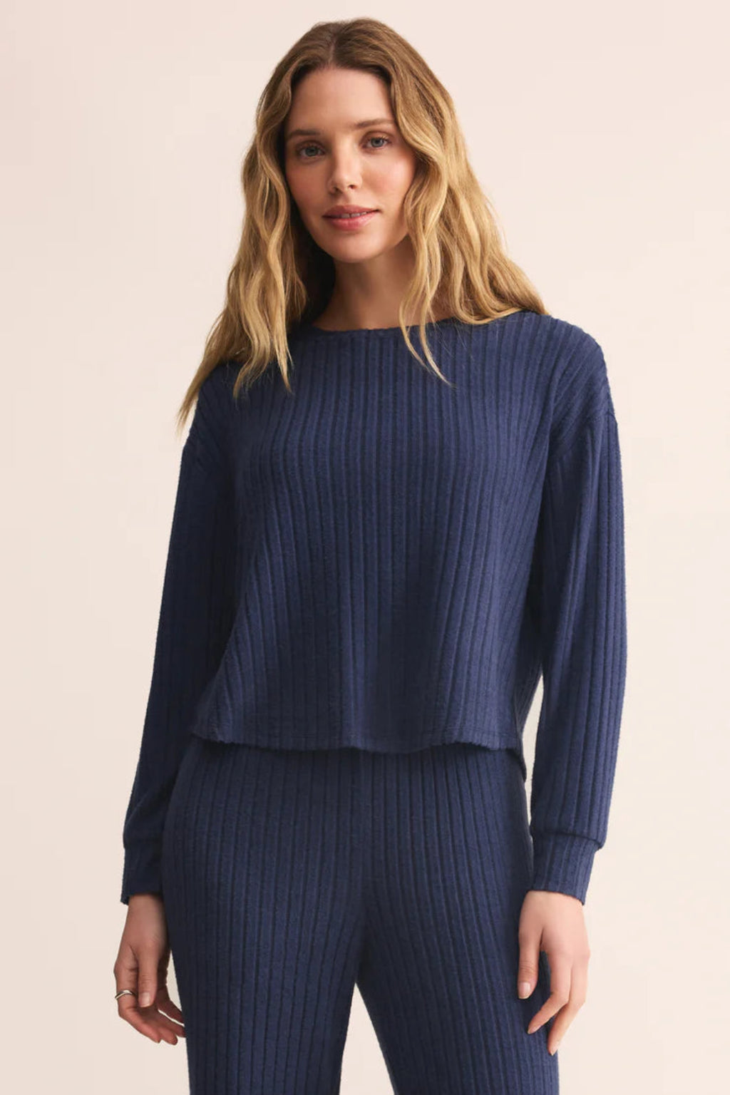 Woman wearing a navy ribbed sweater and pants on a beige background.
