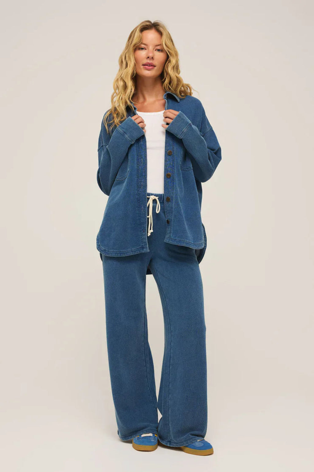 A woman wearing a dark blue button up jacket and a matching pair of pants with blue sneakers.