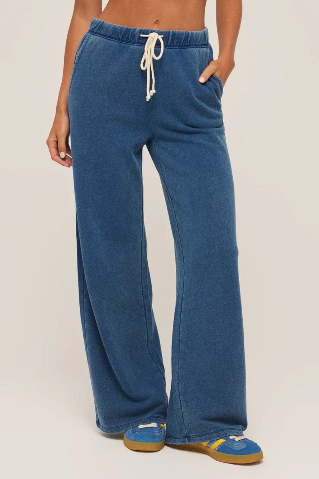 A woman wearing a dark blue pair of pants with blue sneakers.
