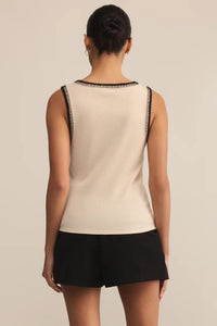 Woman wearing a beige sleeveless top with black trim and black shorts on a beige background.