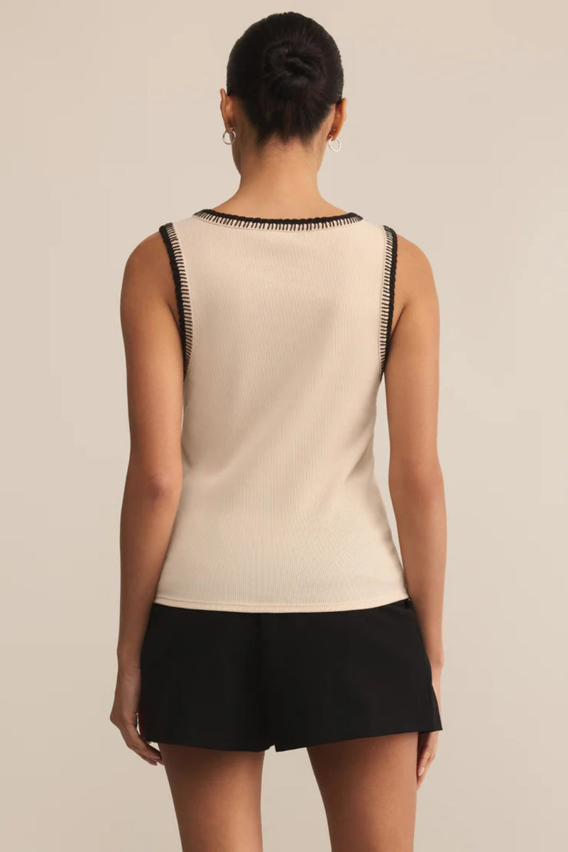 Woman wearing a beige sleeveless top with black trim and black shorts on a beige background.