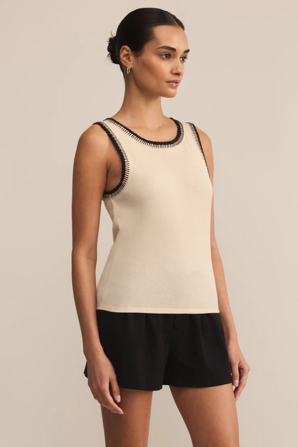 Woman wearing a beige tank top with black trim and black shorts on a beige background.