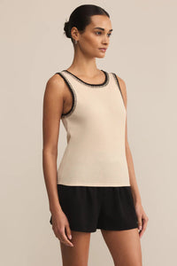 Woman wearing a beige tank top with black trim and black shorts on a beige background.