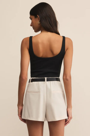 Woman wearing a black tank top and beige shorts on a beige background.