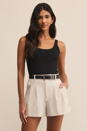 Woman wearing a black sleeveless top and white shorts on a beige background.