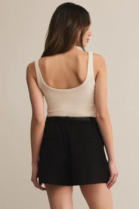 Woman wearing a beige tank top and black skirt on a beige background.
