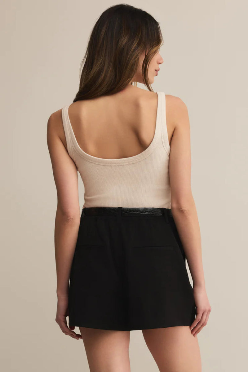 Woman wearing a beige tank top and black skirt on a beige background.