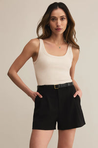 Woman wearing a beige tank top and black shorts against a neutral background.