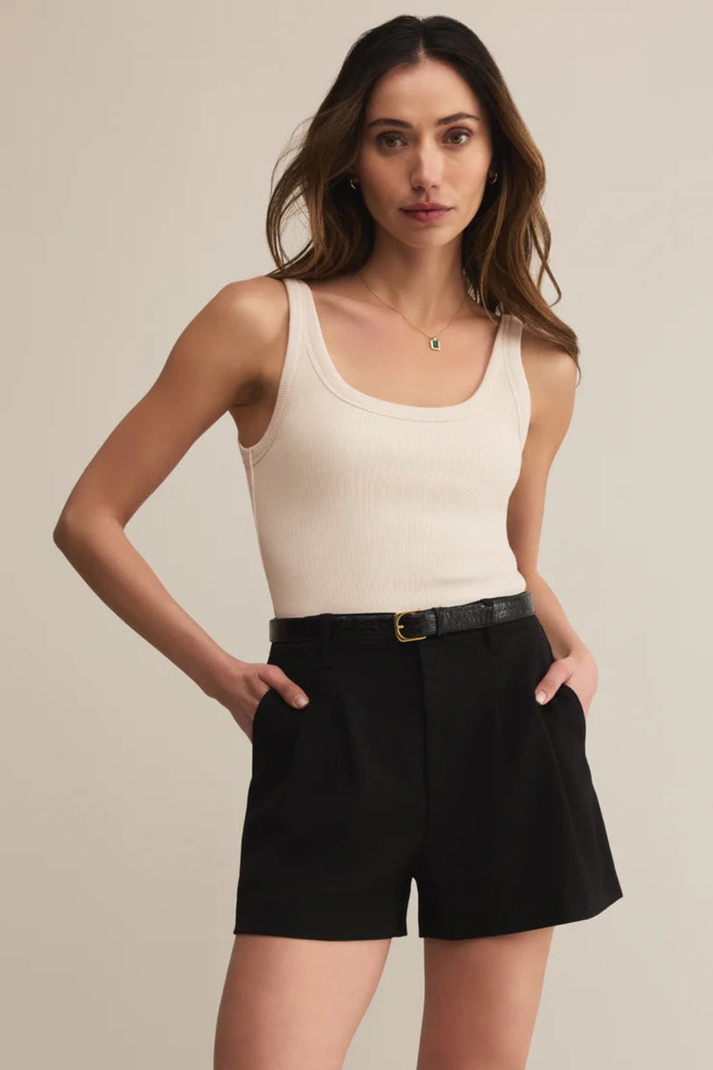 Woman wearing a beige tank top and black shorts against a neutral background.