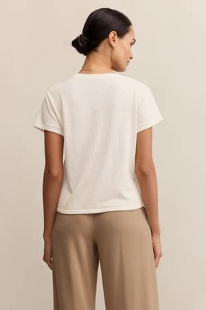 Woman wearing a white t-shirt and beige pants against a plain background.