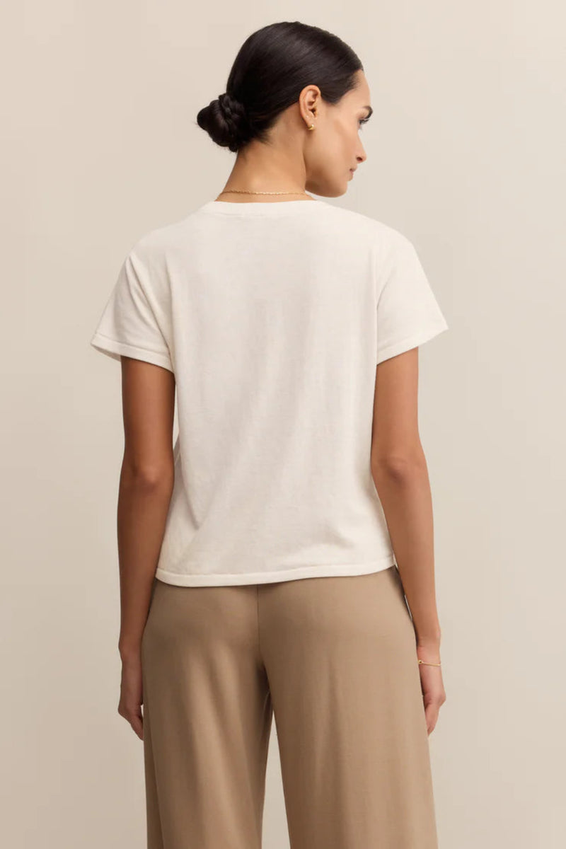 Woman wearing a white t-shirt and beige pants against a plain background.
