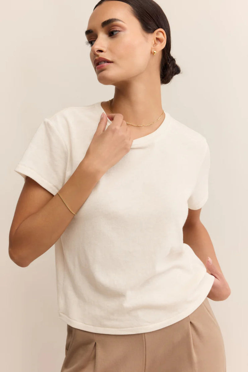 Woman wearing a white top and beige pants against a plain background.