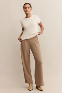 Woman wearing a white top and beige pants on a plain background.