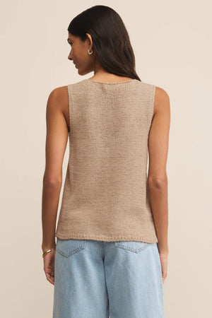 Woman wearing a beige sleeveless top and light blue jeans on a beige background.