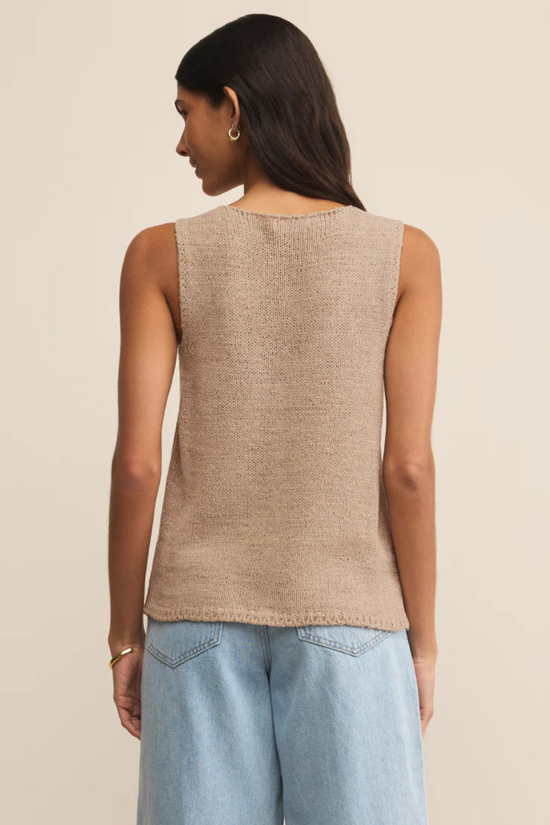 Woman wearing a beige sleeveless top and light blue jeans on a beige background.