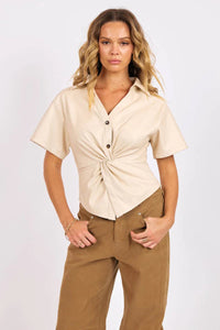 Woman wearing a beige button-up shirt and brown pants on a white background.