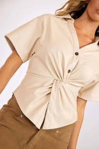 Beige short-sleeve shirt with a knot detail worn by a person on a white background.