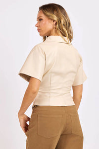Woman wearing a beige short-sleeve shirt and brown pants on a white background.