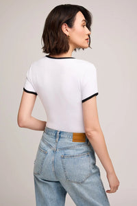 Woman wearing a white t-shirt with black trim and light blue jeans on a plain background.