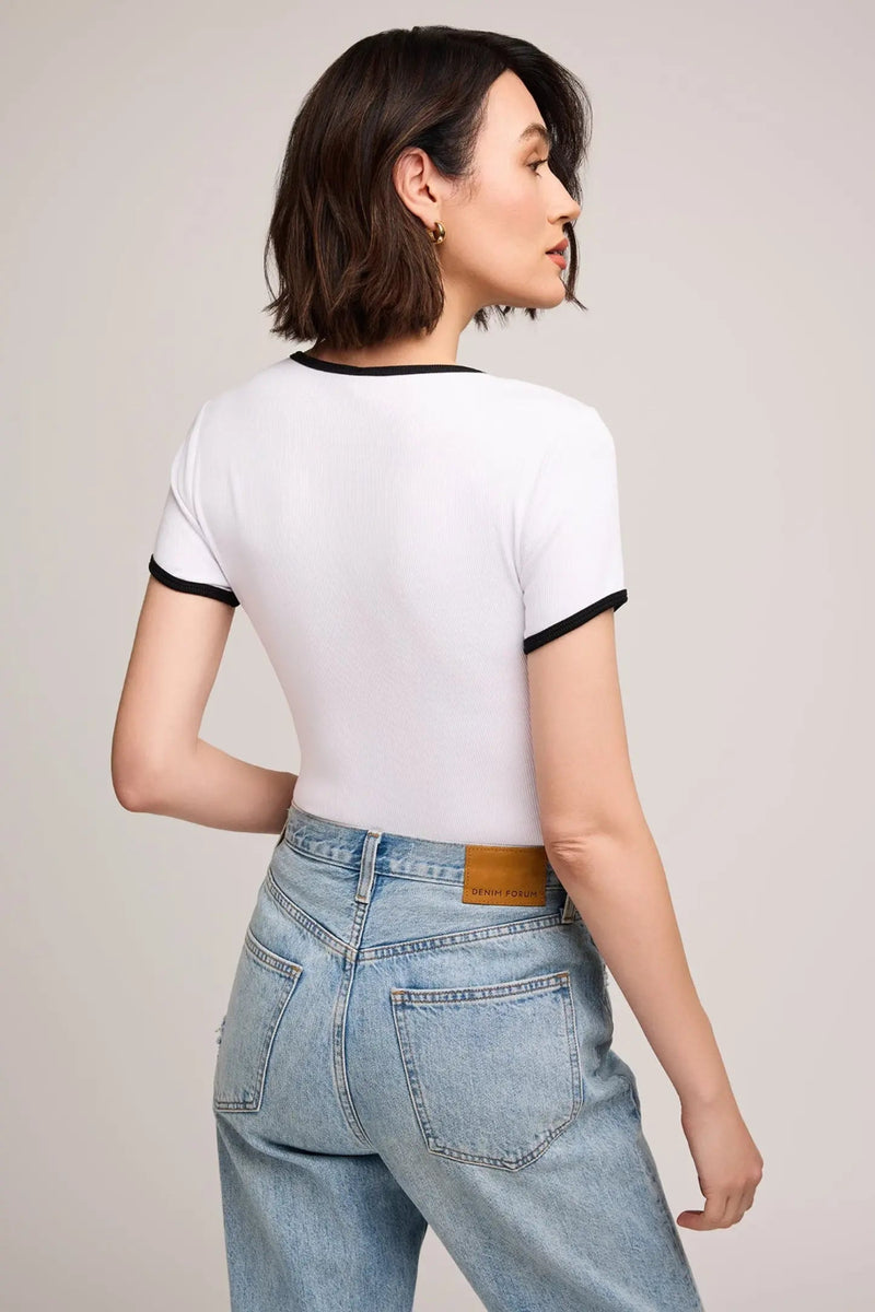 Woman wearing a white t-shirt with black trim and light blue jeans on a plain background.