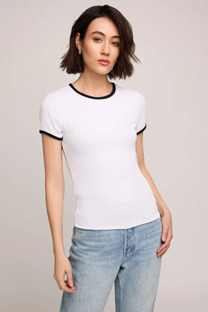 Woman wearing a white t-shirt with black trim and light blue jeans on a plain background.