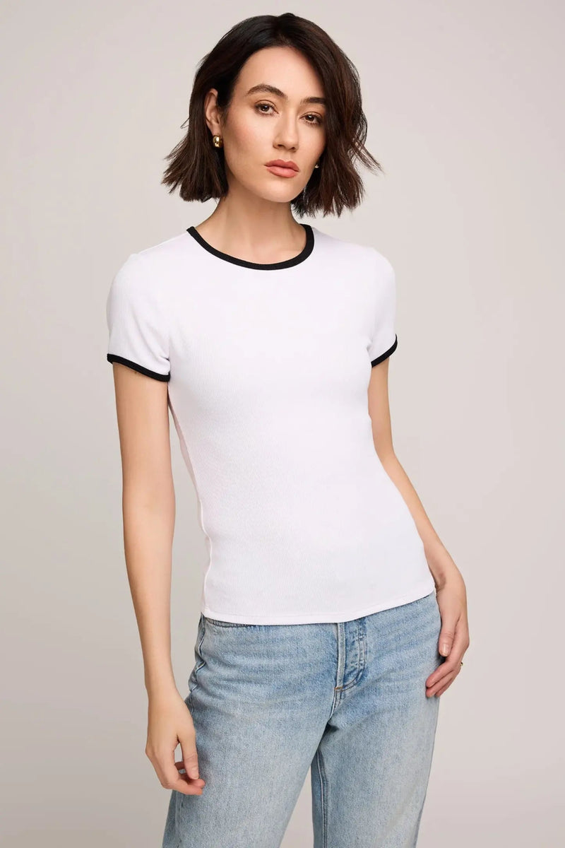 Woman wearing a white t-shirt with black trim and light blue jeans on a plain background.