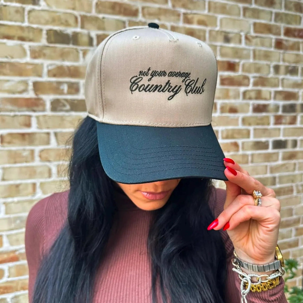 A close up of a woman wearing a trucker hat that says Not Your Average Country Club. 