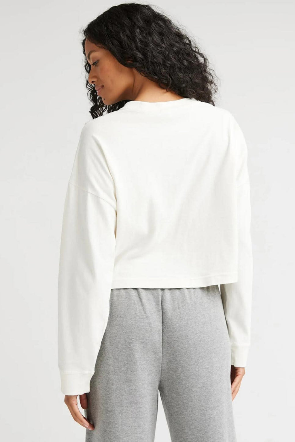 Back view of a woman wearing an off white long sleeve shirt with grey sweatpants.