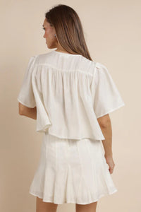 The back view of a woman wearing an ivory shirt with a matching skirt. 