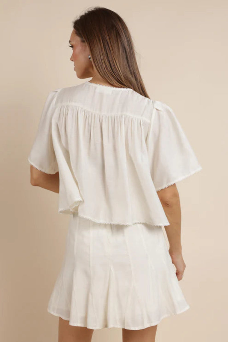 The back view of a woman wearing an ivory shirt with a matching skirt. 