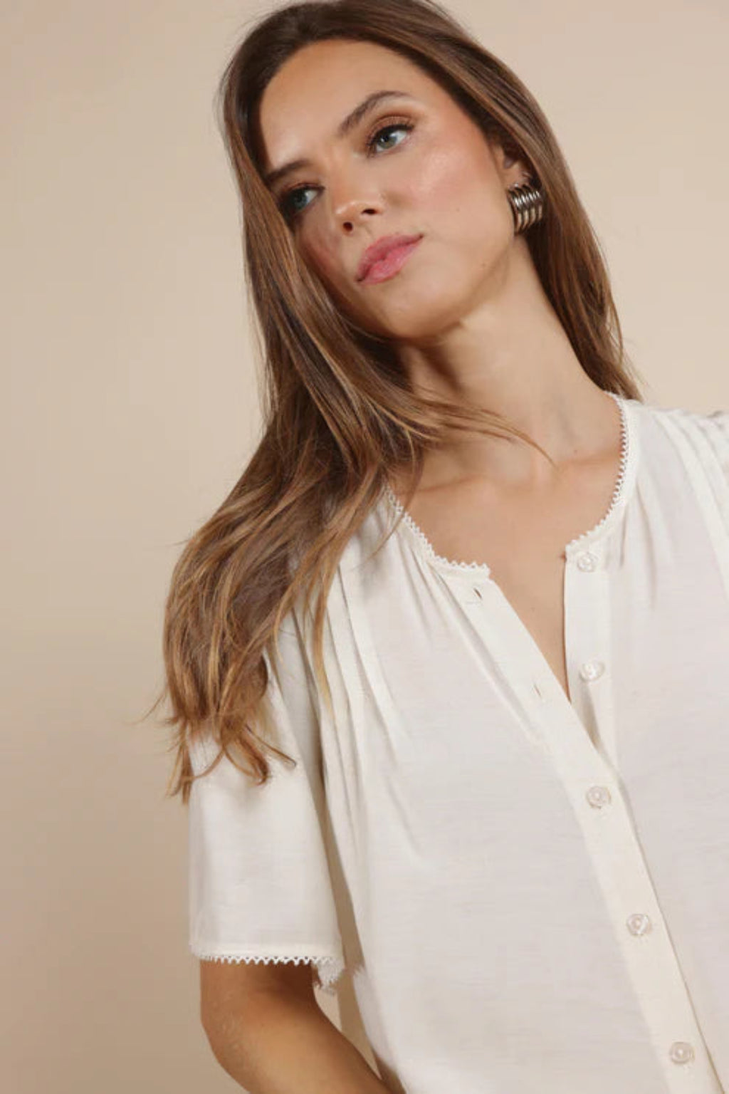 A close up of a woman wearing an ivory button up shirt. 