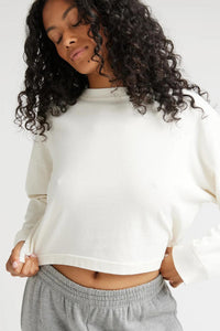 Woman wearing an off white long sleeve shirt with grey sweatpants.